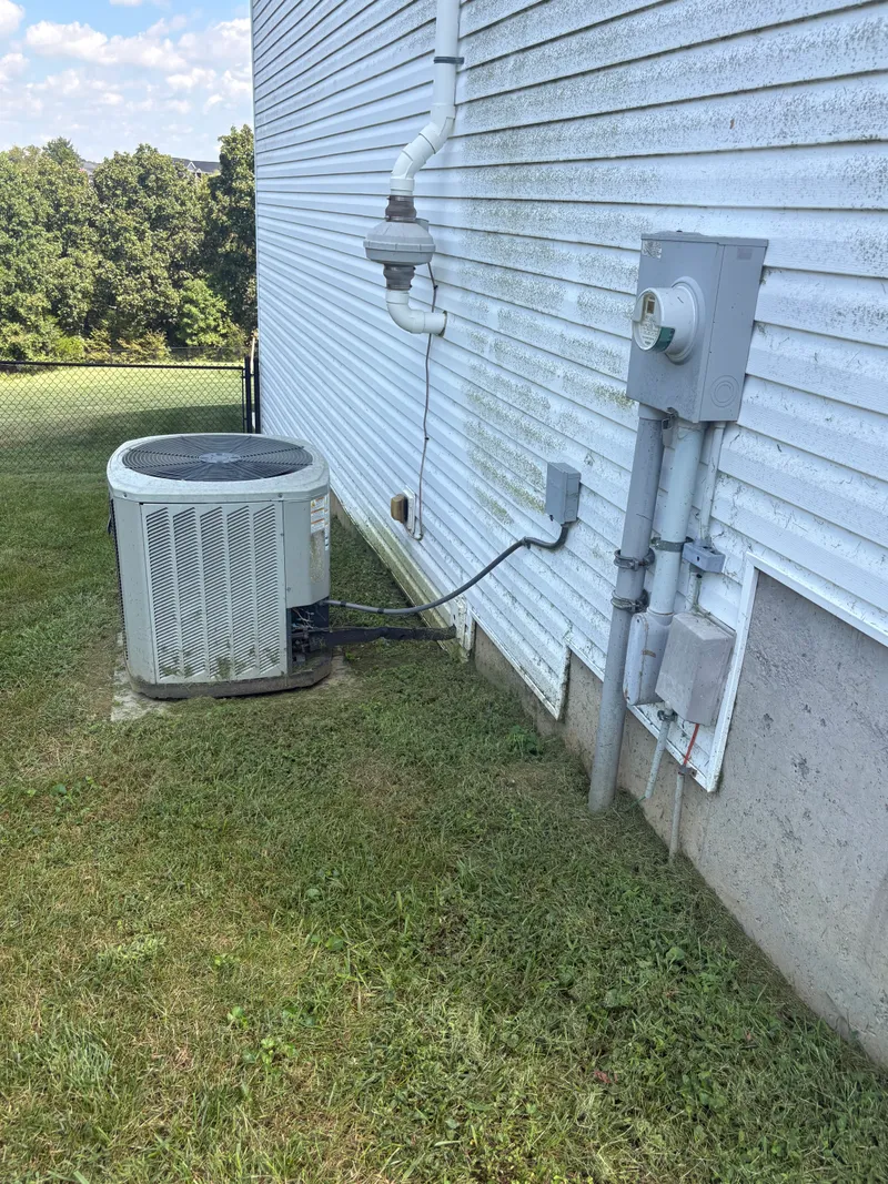 Before cleaning: vinyl siding streaked with green growth, a vent pipe and electrical box on the wall, and an AC unit in the grass below.