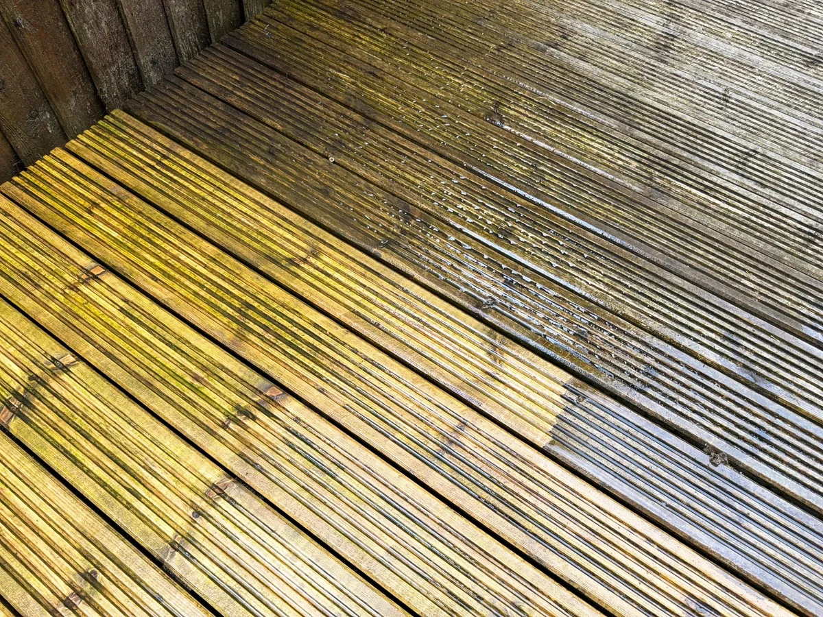 Wood deck boards split between dark algae-covered wood and bright freshly cleaned wood