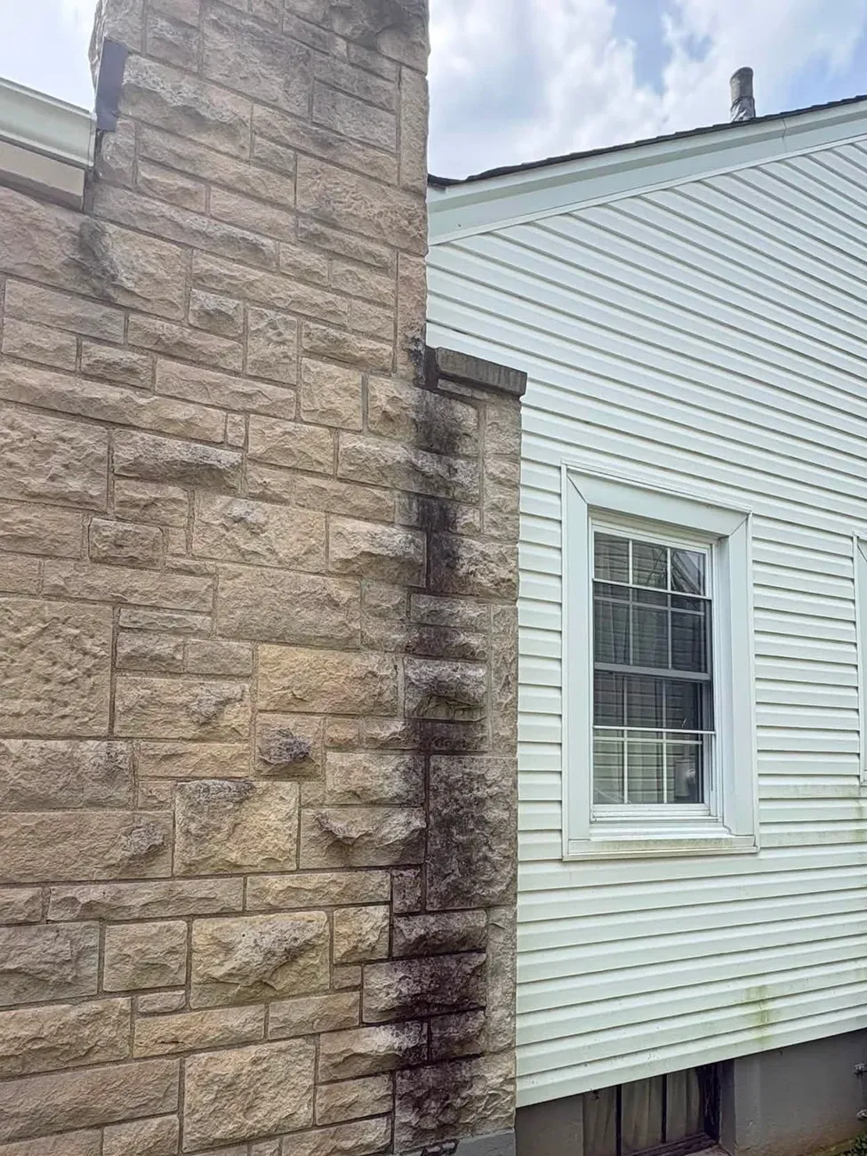 Before: tan stone chimney with dark black streaks down one edge, beside white vinyl siding and a window