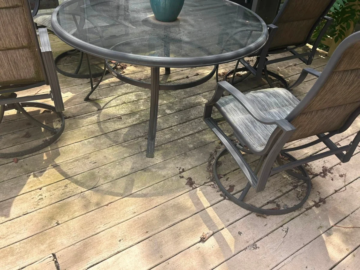 Before: weathered gray wood deck boards with a green tint and leaves, under a glass patio table and chairs