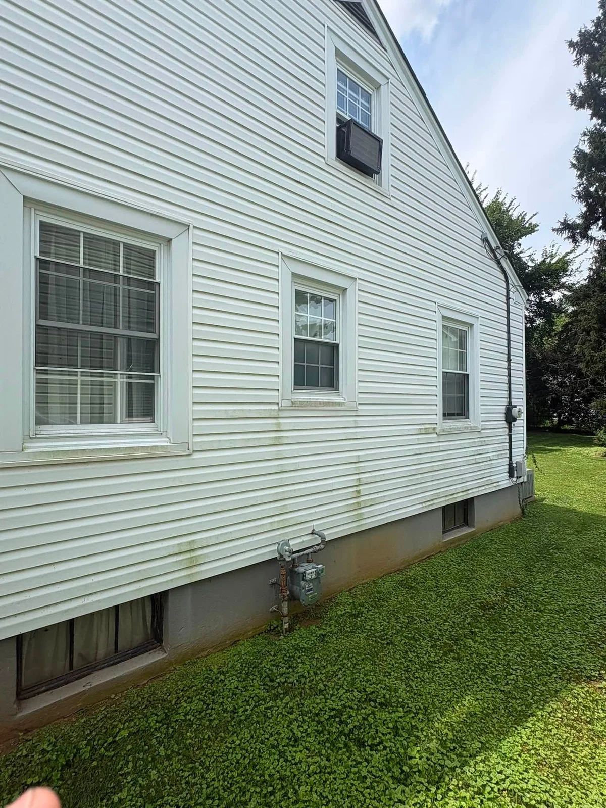 After: white vinyl siding on a house side wall with windows, a gas meter and a basement window above a grassy yard