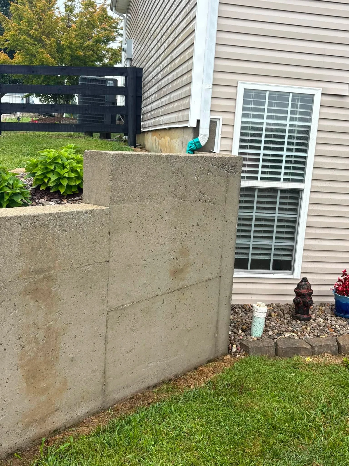 After: lighter, even concrete retaining wall beside the house, with a rock bed and plants on top