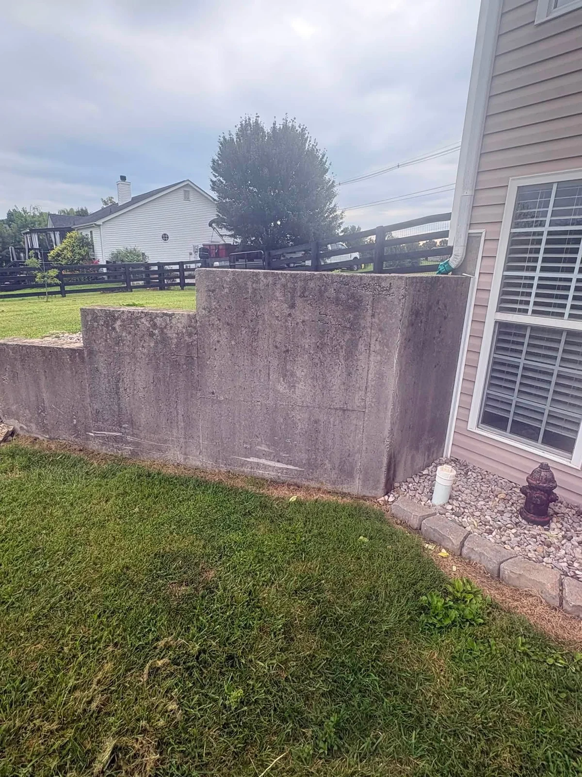 Before: gray concrete retaining wall beside a house, dark with stains and grime
