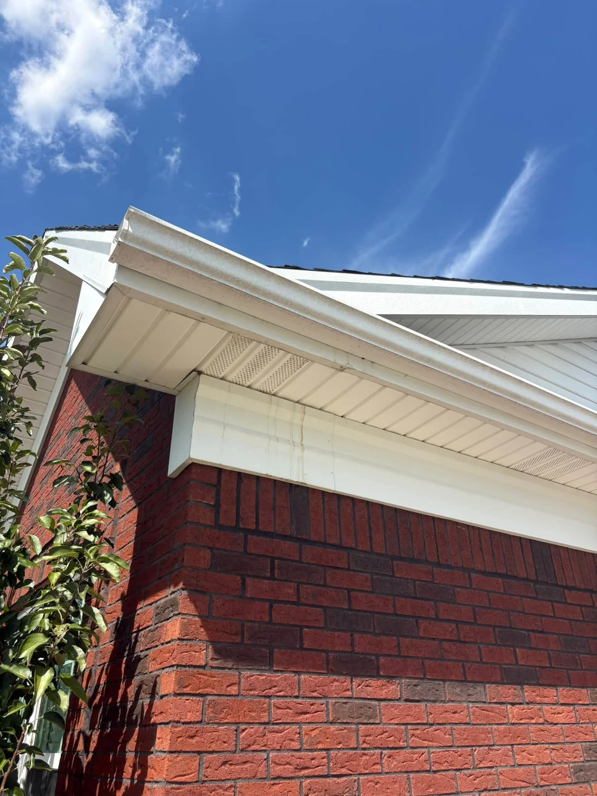 After: white gutter, fascia and vented soffit above a red brick wall, under a blue sky