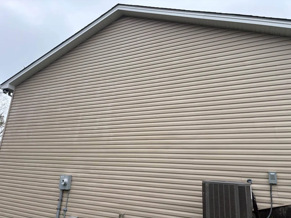 After: tan vinyl siding on a gabled house wall, with an electric meter and an air conditioner unit at the base