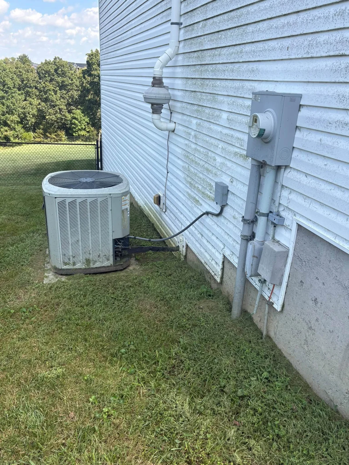 Before: white vinyl siding with green speckled algae around a vent pipe, electric meter and air conditioner unit