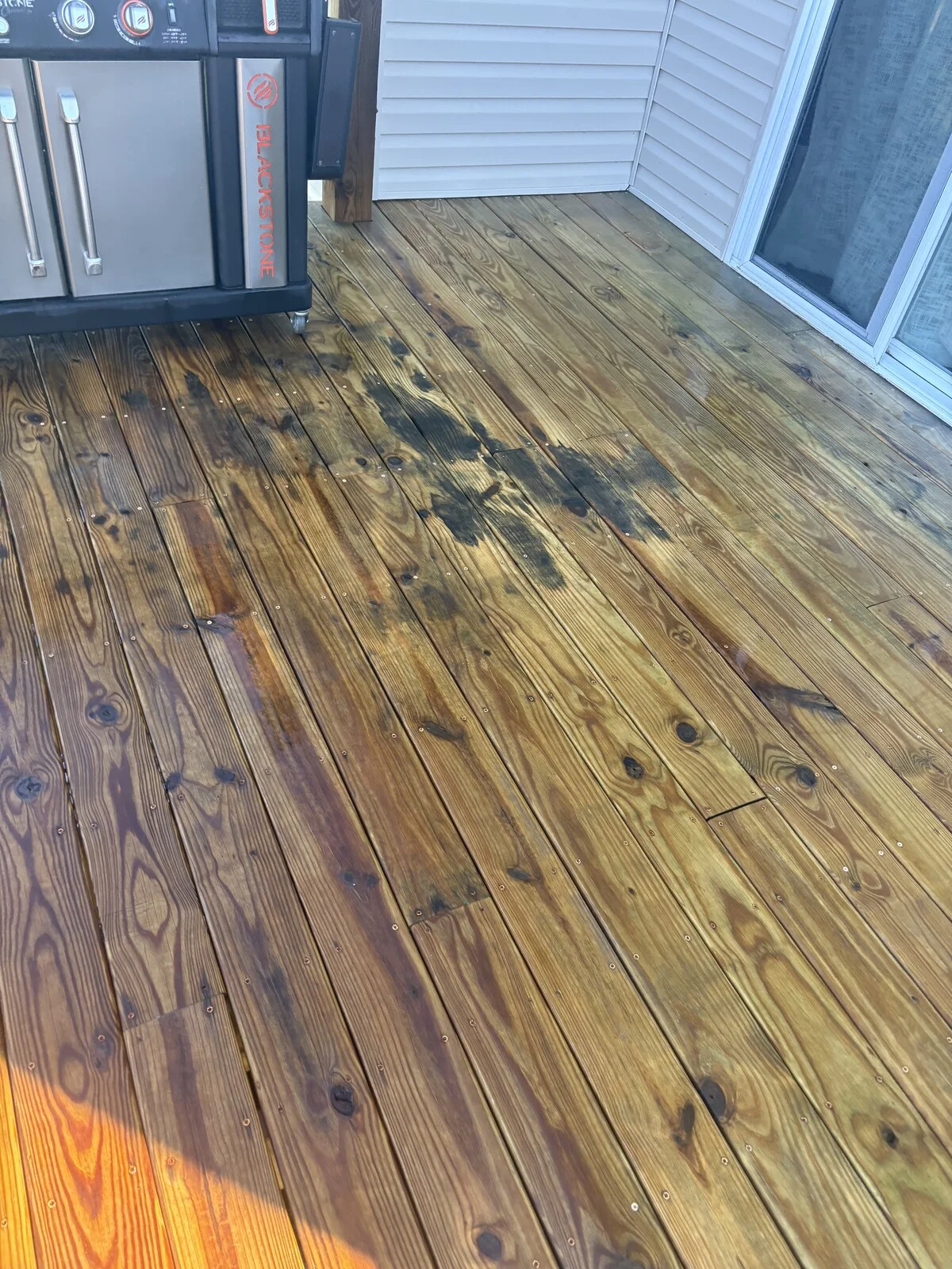 After: the same deck in golden brown wood from the same spot, with dark patches still visible near the grill, beside vinyl siding