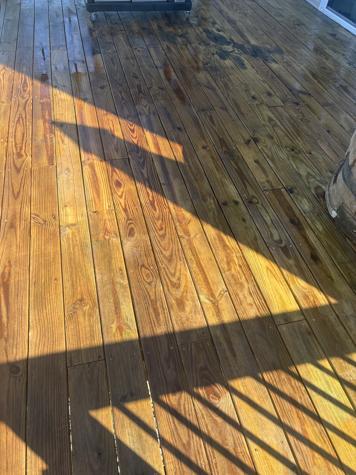 After: wet golden brown deck boards with grain showing and railing shadows across them, with a few dark patches near the top