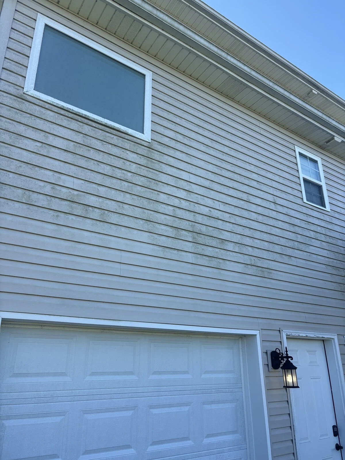 Before: beige vinyl siding above a white garage door with green streaks under a large window and a smaller window at right