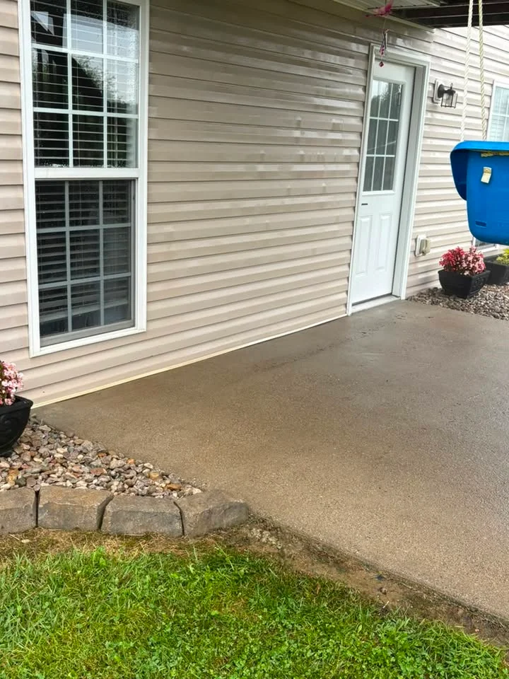 After: concrete patio beside tan vinyl siding and a white door, with flower pots, a gravel bed and a stone edge