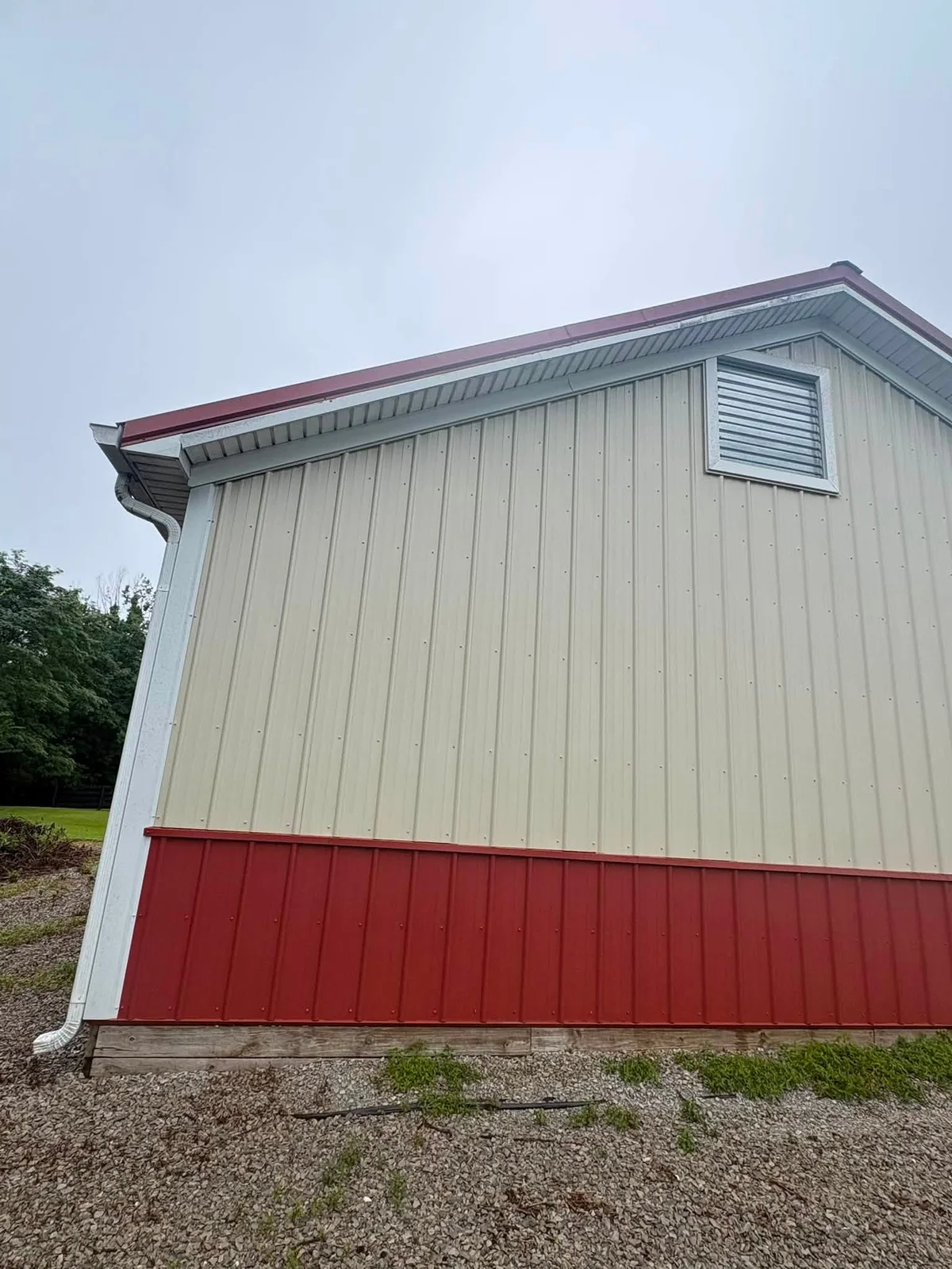 After: beige metal pole building wall with a red lower panel, white gutter and a louvered gable vent