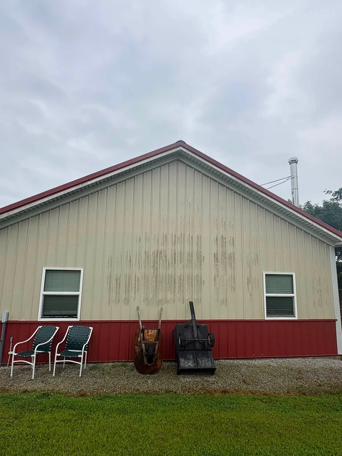 Before: beige metal pole building wall with dark vertical streaks above a red lower panel, chairs and a wheelbarrow in front